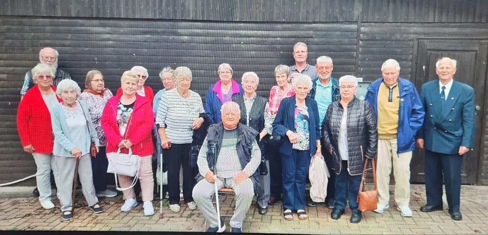 Große Gruppe von Klienten beim gemeinsamen Gruppenfoto vor einer Holzwand