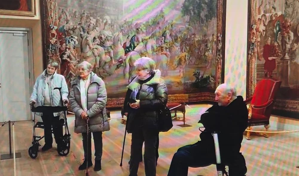 Klienten mit Rollator und Gehstock vor einem großen Wandteppich bei einem Museumsbesuch
