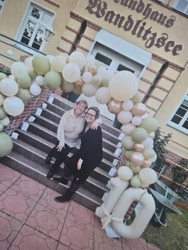 Zwei Mitarbeiterinnen auf der Treppe des Landhauses vor einer Ballongirlande mit der Zahl 10