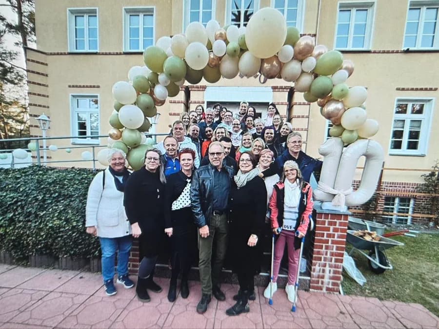 Gruppenfoto des Teams unter dem Ballonbogen mit der Zahl 10 vor dem Landhaus
