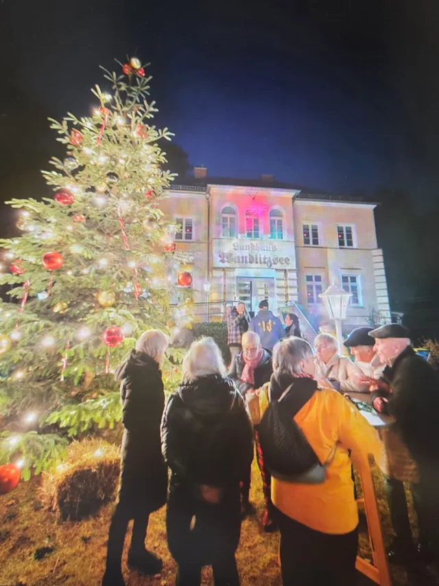 Gäste am Stehtisch vor dem beleuchteten Landhaus Wandlitzsee und dem Weihnachtsbaum