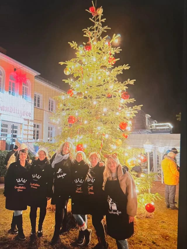 Sechs Frauen in schwarzen Schürzen vor dem beleuchteten Weihnachtsbaum am Landhaus Wandlitzsee